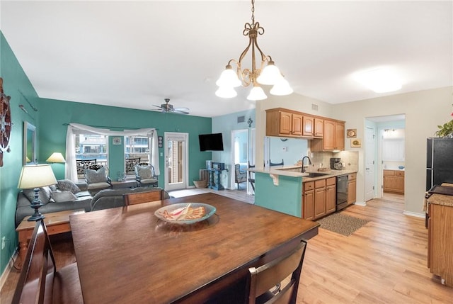 dining space with sink, ceiling fan with notable chandelier, and light hardwood / wood-style floors