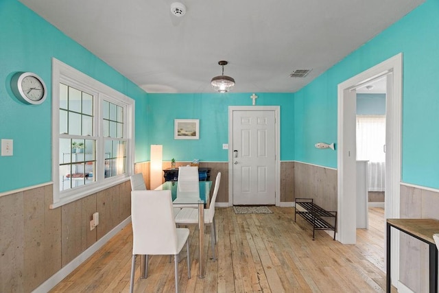 dining space featuring light wood-style floors, visible vents, wood walls, and wainscoting