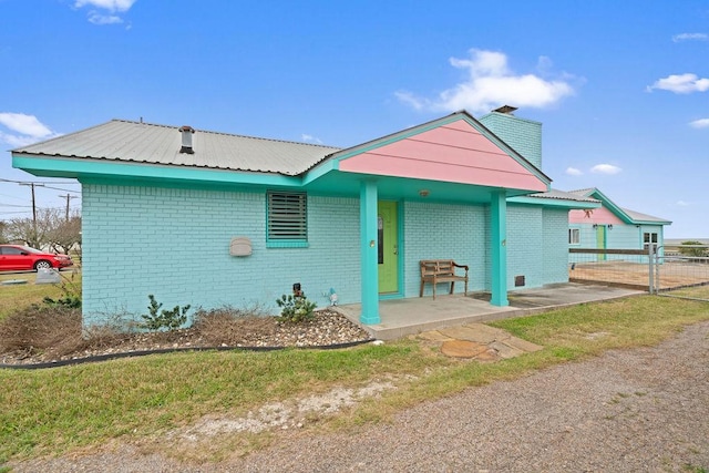 view of front facade featuring covered porch, metal roof, brick siding, and a chimney