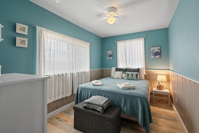 bedroom featuring light wood-type flooring, wooden walls, and wainscoting