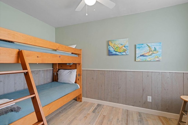 bedroom with a wainscoted wall, light wood finished floors, wood walls, and a ceiling fan