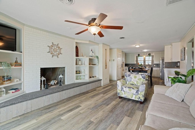 living area with ceiling fan, light wood-type flooring, a fireplace, and visible vents