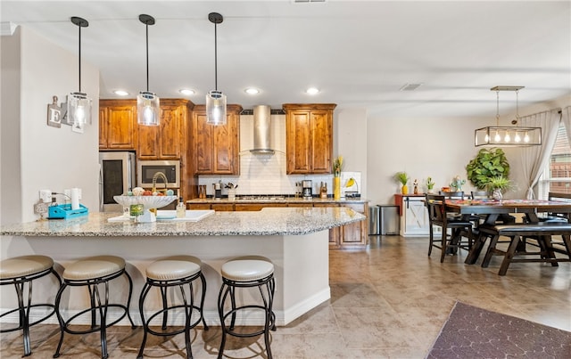 7622 Neches Dr, Corpus Christi, TX 78414 - kitchen featuring appliances with stainless steel finishes, wall chimney exhaust hood, brown cabinets, a breakfast bar, and recessed lighting