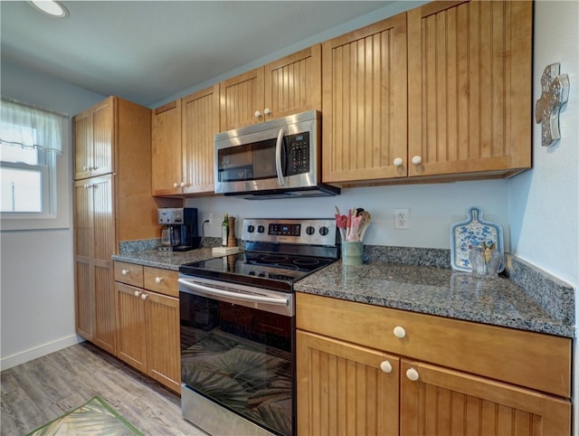 kitchen with stainless steel appliances, dark stone countertops, and light hardwood / wood-style flooring