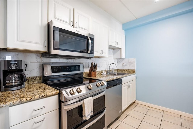 kitchen featuring sink, light tile patterned floors, light stone countertops, appliances with stainless steel finishes, and white cabinetry