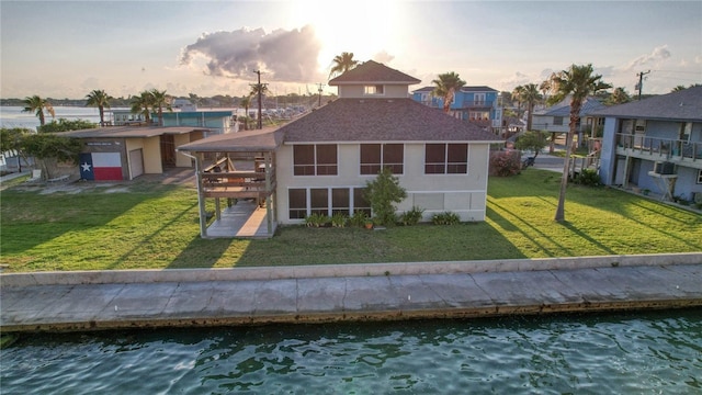 back house at dusk with a lawn and a water view