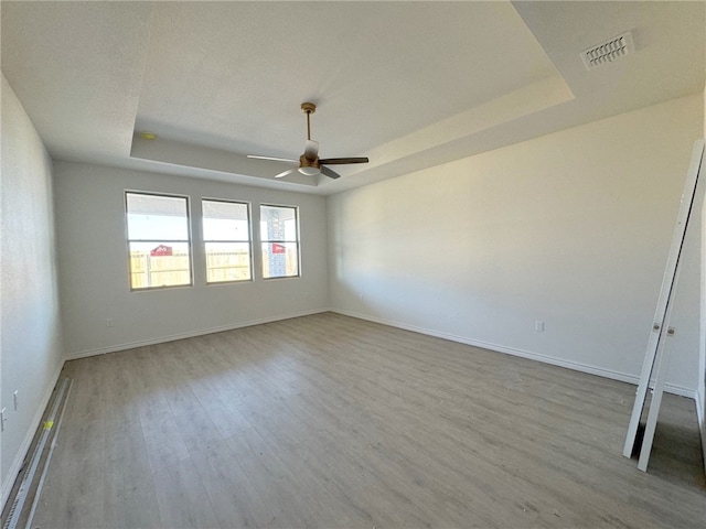 empty room with light hardwood / wood-style floors, ceiling fan, and a tray ceiling