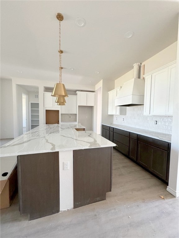 kitchen featuring white cabinetry, hanging light fixtures, backsplash, a kitchen island, and light wood-type flooring