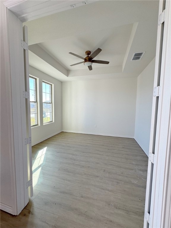 unfurnished room with ceiling fan, light hardwood / wood-style floors, and a raised ceiling