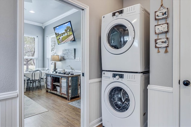 clothes washing area with stacked washer and dryer, light hardwood / wood-style flooring, and crown molding