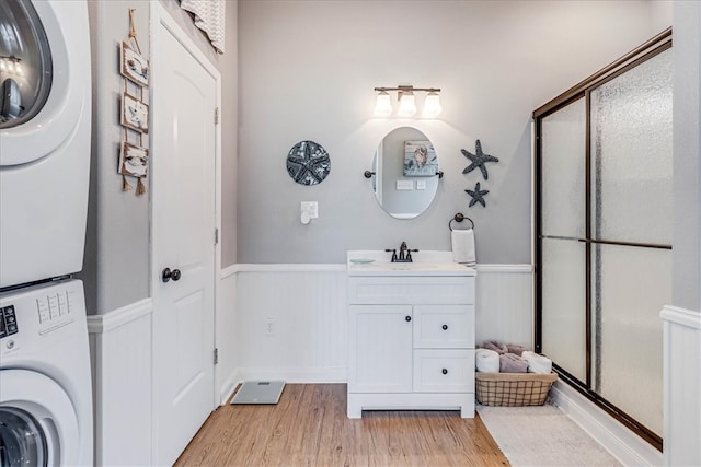 bathroom with hardwood / wood-style floors, a shower with shower door, vanity, and stacked washer / dryer