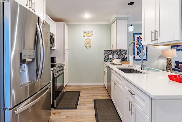 kitchen with appliances with stainless steel finishes, decorative light fixtures, sink, white cabinets, and ornamental molding