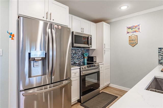 kitchen featuring white cabinetry, crown molding, light stone counters, light hardwood / wood-style flooring, and appliances with stainless steel finishes