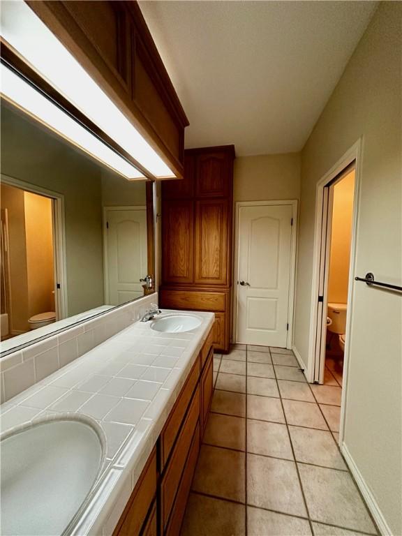 bathroom featuring toilet, double vanity, a sink, and tile patterned floors