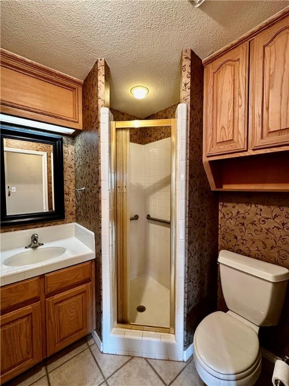 bathroom featuring toilet, vanity, a shower stall, a textured ceiling, and wallpapered walls