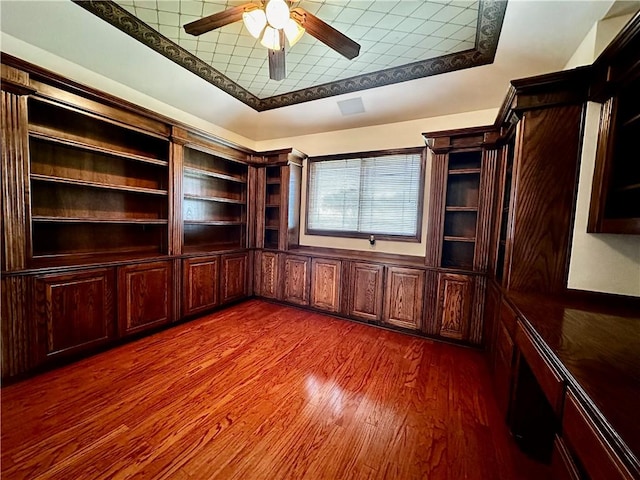 unfurnished office featuring ceiling fan, a tray ceiling, and dark wood-style flooring