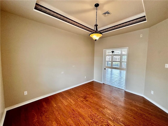 spare room featuring a tray ceiling, visible vents, ornamental molding, wood finished floors, and baseboards