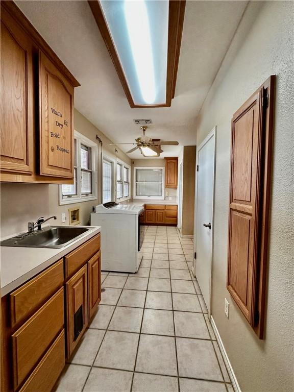 kitchen with visible vents, brown cabinetry, washing machine and clothes dryer, a sink, and light tile patterned flooring