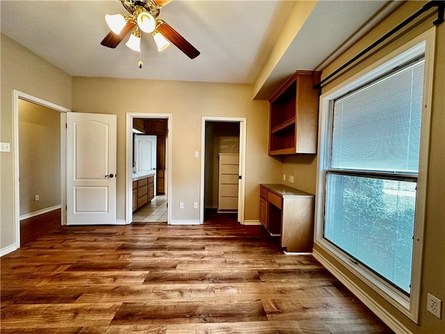 interior space with ensuite bathroom, wood finished floors, a ceiling fan, and baseboards