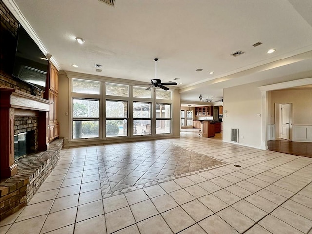 unfurnished living room with light tile patterned floors, ceiling fan, visible vents, ornamental molding, and a brick fireplace