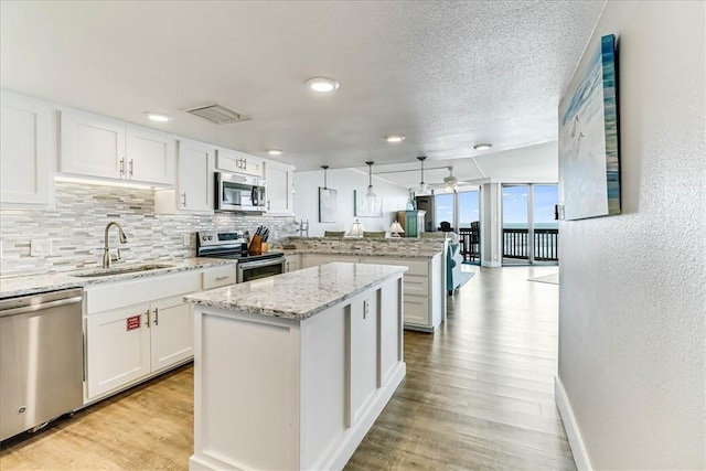kitchen featuring white cabinets, appliances with stainless steel finishes, a sink, a peninsula, and backsplash