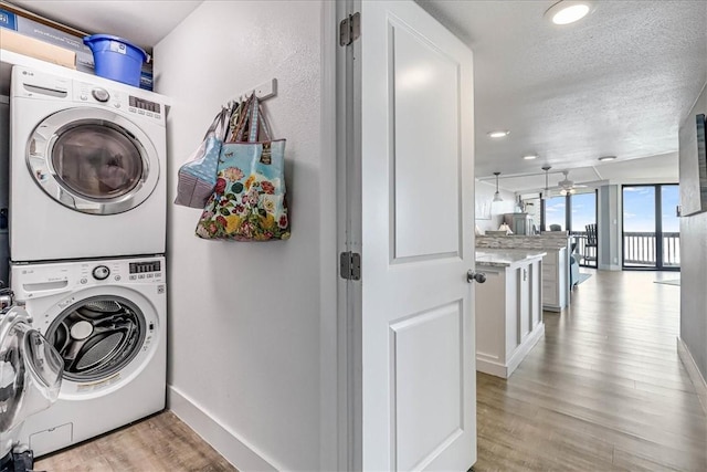 laundry room featuring laundry area, stacked washer and clothes dryer, light wood-style floors, and baseboards