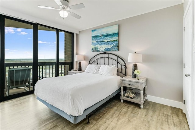 bedroom with a ceiling fan, baseboards, a wall of windows, and wood finished floors