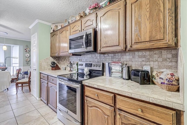 kitchen with crown molding, light tile patterned floors, a textured ceiling, appliances with stainless steel finishes, and tile counters