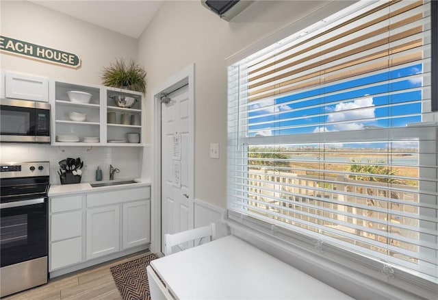 kitchen featuring appliances with stainless steel finishes, sink, white cabinets, decorative backsplash, and light hardwood / wood-style flooring