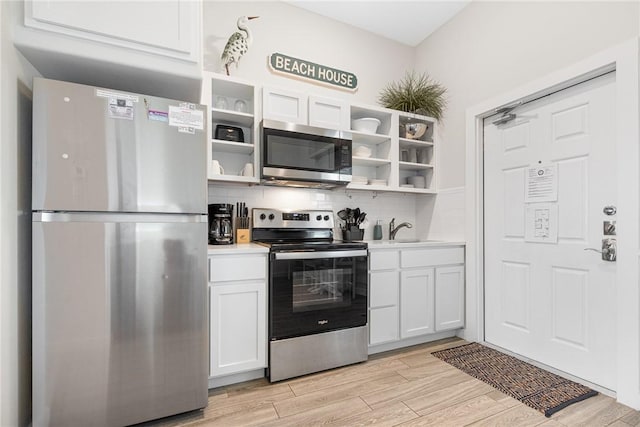 kitchen featuring sink, white cabinetry, light wood-type flooring, appliances with stainless steel finishes, and backsplash