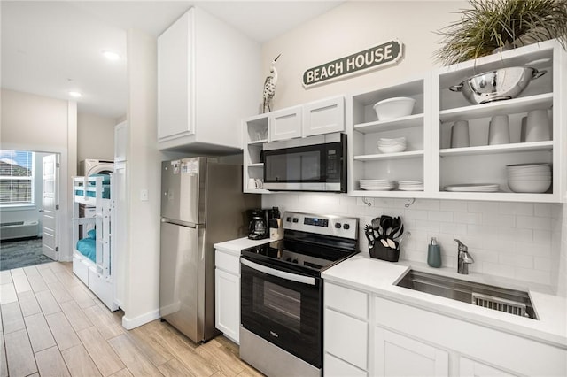 kitchen with stainless steel appliances, sink, white cabinets, and light hardwood / wood-style flooring