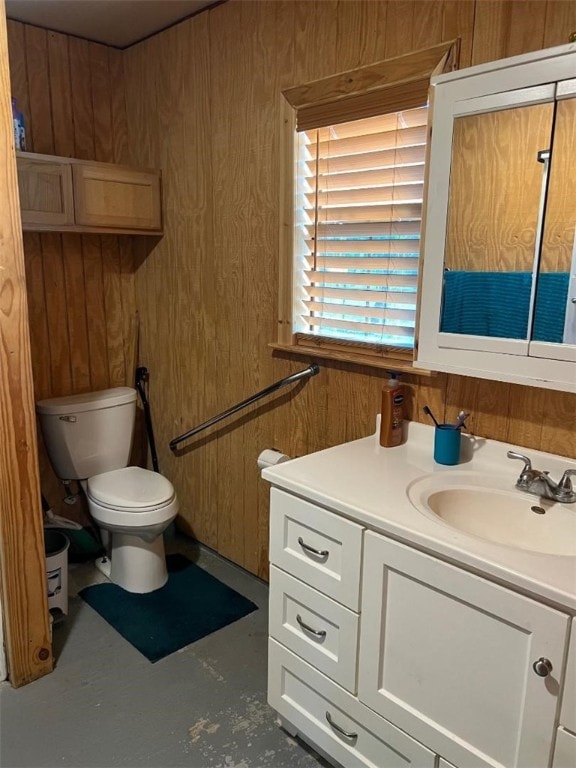 bathroom featuring toilet, wood walls, vanity, and concrete flooring