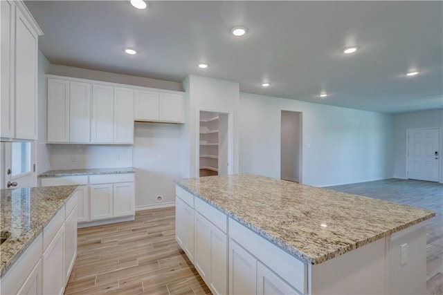 kitchen featuring a kitchen island, light stone counters, and white cabinetry