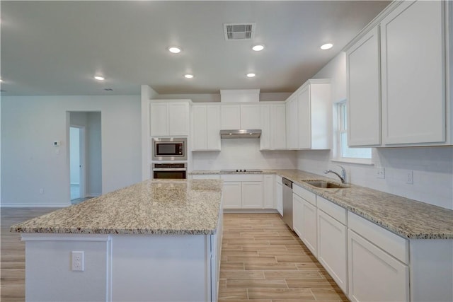 kitchen featuring sink, white cabinets, a center island, light stone counters, and appliances with stainless steel finishes