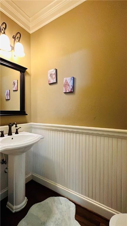 14890 Granada Dr Unit 107, Corpus Christi, TX 78418 - half bathroom featuring a wainscoted wall, ornamental molding, wood finished floors, a sink, and toilet