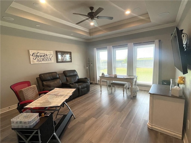 living area featuring a raised ceiling, ornamental molding, wood finished floors, baseboards, and ceiling fan