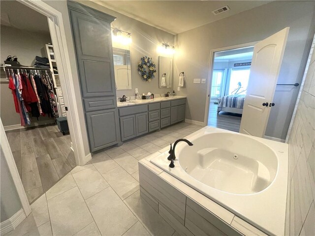 full bathroom featuring visible vents, a sink, double vanity, a spacious closet, and a whirlpool tub