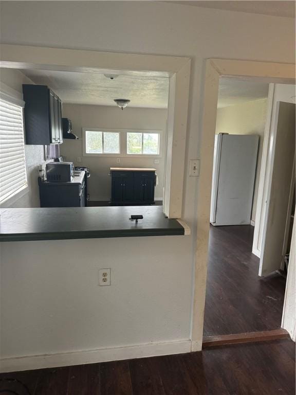 kitchen featuring white fridge, dark hardwood / wood-style flooring, kitchen peninsula, and extractor fan