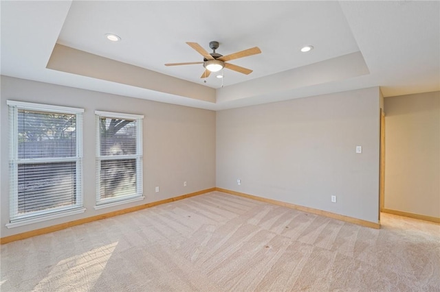 empty room featuring light carpet, a raised ceiling, and ceiling fan