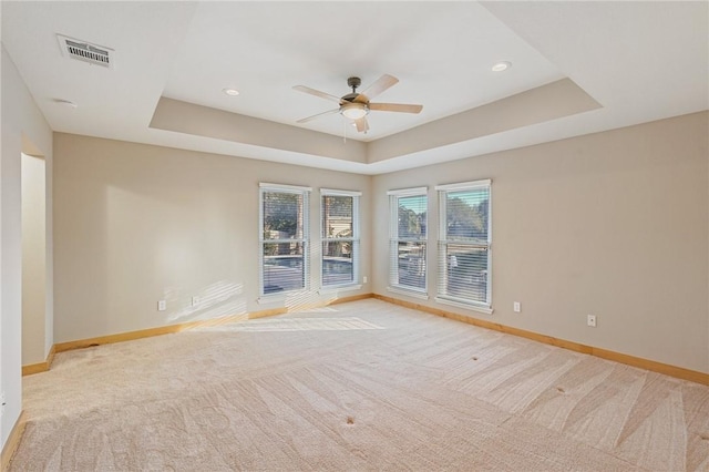 carpeted spare room with a raised ceiling and ceiling fan