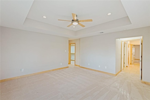 empty room with a raised ceiling, light colored carpet, and ceiling fan