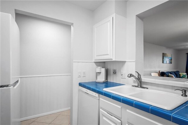 kitchen with tile countertops, white cabinetry, sink, light tile patterned floors, and white appliances