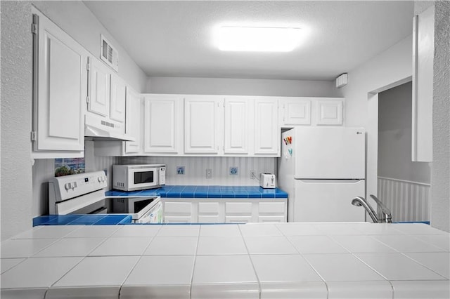 kitchen featuring white cabinetry, a textured ceiling, sink, tile counters, and white appliances