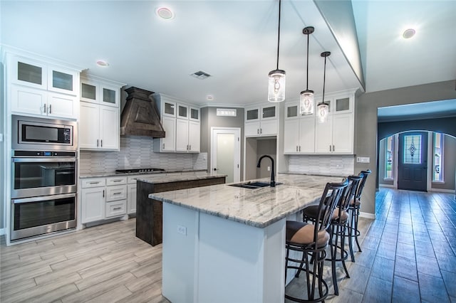 kitchen with a center island with sink, white cabinets, hanging light fixtures, sink, and light stone countertops