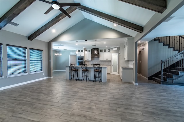 kitchen with white cabinets, hanging light fixtures, a kitchen island with sink, light hardwood / wood-style flooring, and premium range hood