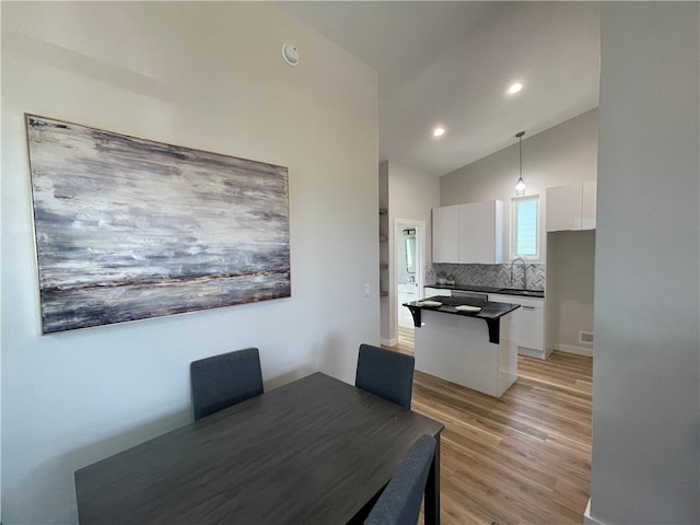 dining space with light wood-type flooring, sink, and vaulted ceiling