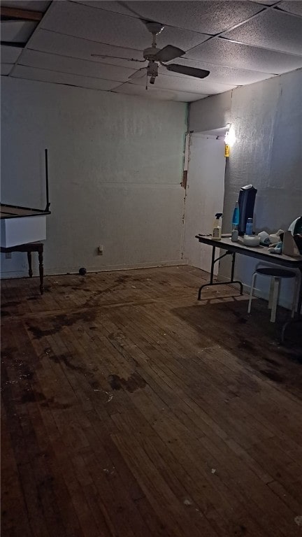 basement with a paneled ceiling, wood-type flooring, and ceiling fan