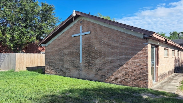 view of property exterior with fence, a lawn, and brick siding