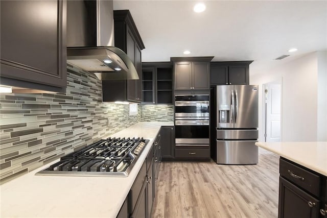 13765 Eaglesnest Bay Dr, Corpus Christi, TX 78418 - kitchen featuring appliances with stainless steel finishes, wall chimney range hood, light countertops, tasteful backsplash, and light wood-style flooring