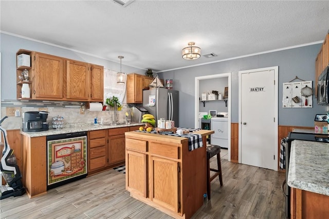 kitchen with stainless steel fridge, light wood-type flooring, range, washing machine and dryer, and hanging light fixtures